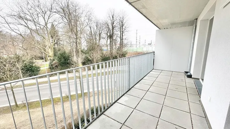 Geräumiger Balkon mit Fliesenboden und Blick auf die umliegende Grünfläche und Bäume.
