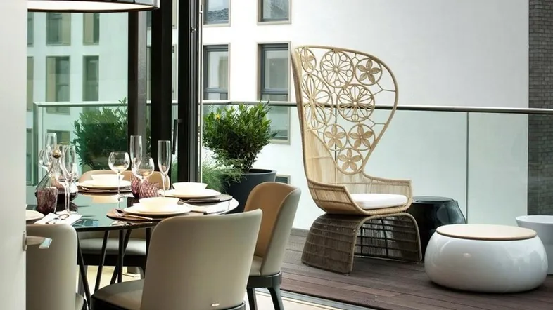 Moderner Essbereich mit elegantem Glastisch und Zugang zu einem möblierten Balkon mit Rattanmöbeln.