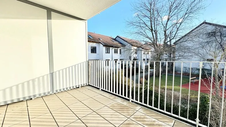 Geräumiger Balkon mit Fliesenboden und Blick auf den gemeinschaftlichen Innenhof mit Spielplatz.