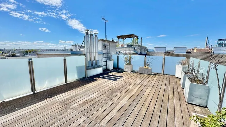 Geräumige Dachterrasse mit Holzboden, Glasgeländer und weitem Blick über die Stadt.