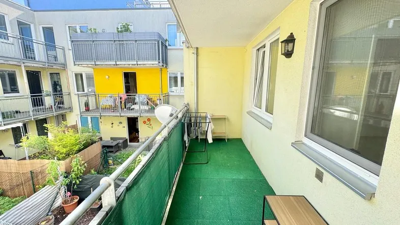 Heller Balkon mit grünem Bodenbelag und Blick auf den ruhigen Innenhof der Wohnanlage.
