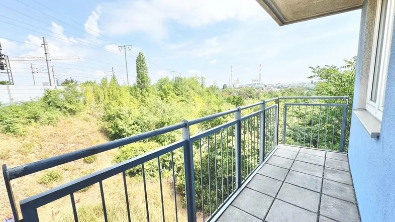 Geräumiger Balkon mit Fliesenboden und weitem Blick ins Grüne unter blauem Himmel.
