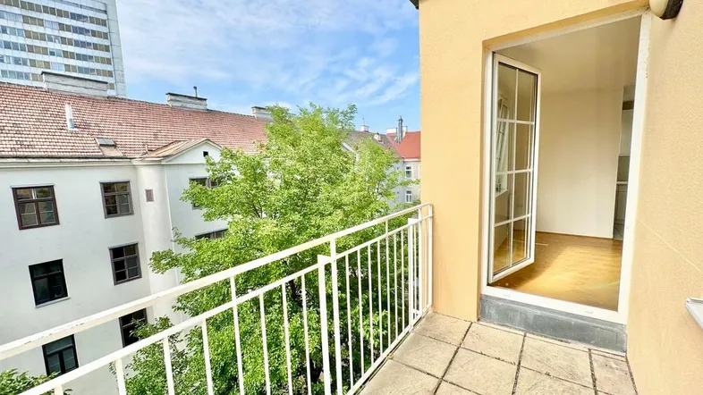 Geräumiger Balkon mit Fliesenboden und Blick auf den begrünten Innenhof sowie angrenzende Gebäude.