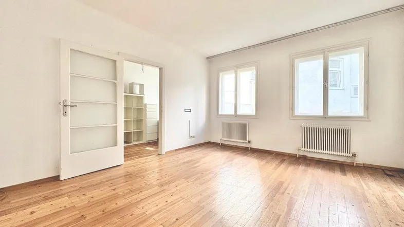 Helles Zimmer mit Holzboden, weißen Wänden und Fenstern, die viel Tageslicht hereinlassen.