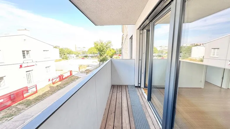 Heller Balkon mit Holzboden und Blick auf die Umgebung, zugänglich durch große Glasschiebetüren.