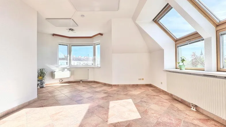 Helles Dachzimmer mit Fliesenboden, Erkerfenster und Dachfenstern, ideal als Wohnraum.
