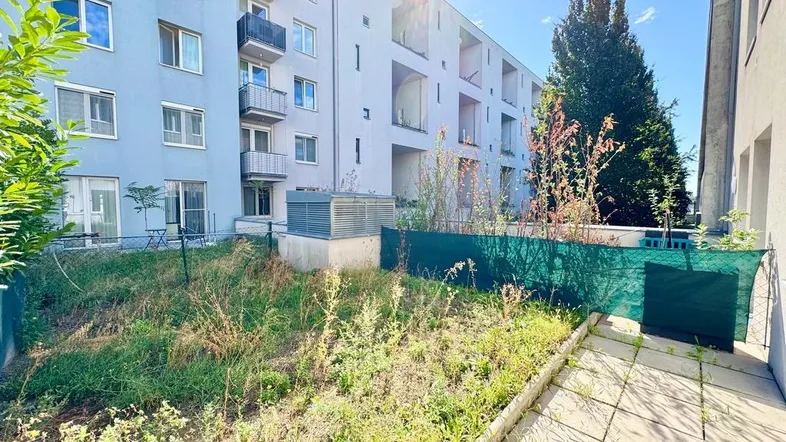 Außenansicht eines modernen Wohngebäudes mit Balkonen und einem ungepflegten Gartenbereich im Vordergrund.