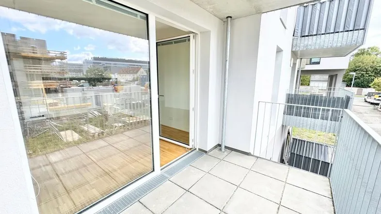 Heller Balkon mit Fliesenboden und Blick auf die Umgebung sowie angrenzende Baustellen.