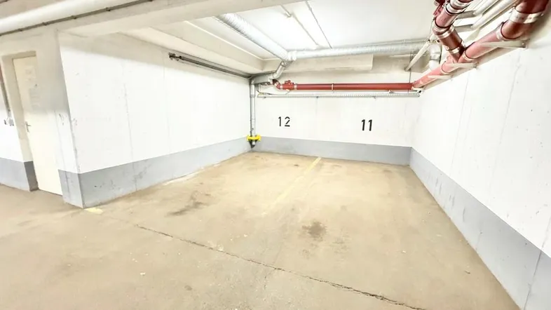 Heller Tiefgaragenstellplatz mit Betonboden und sichtbaren Leitungen an der Decke, gut gepflegt.