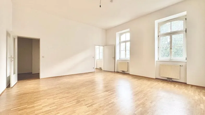Helles, leeres Zimmer mit Parkettboden und zwei großen Fenstern, bereit zur individuellen Gestaltung.