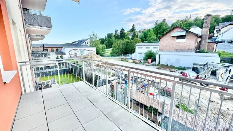 Geräumiger Balkon mit Fliesenboden und Blick auf die umliegende Bebauung und grüne Hügel.