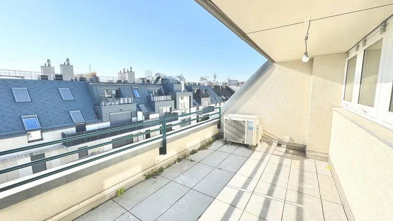 Sonniger Balkon mit Fliesenboden und Blick über die Dächer der Stadt.