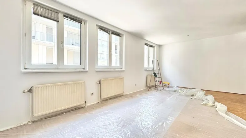 Heller Wohnraum mit frisch gestrichenen Wänden, Holzfußboden und großen Fenstern, bereit zur Einrichtung.