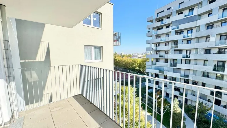 Heller Balkon mit Blick auf moderne Wohngebäude und grüne Umgebung unter blauem Himmel.