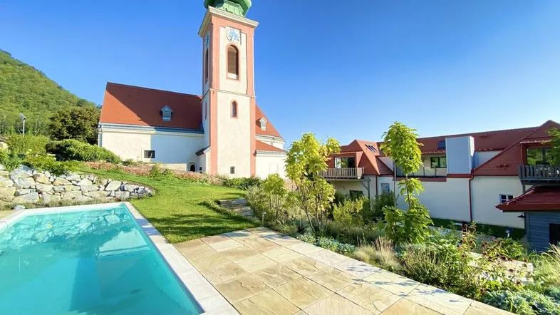 Außenbereich mit großem Pool, gepflegtem Garten und Blick auf die historische Kirche und die umliegenden Hügel.