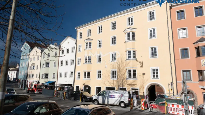Gelbes historisches Gebäude mit vielen Fenstern und einem Torbogen an einer belebten Stadtstraße.