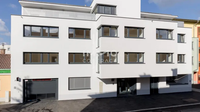 Modernes Mehrfamilienhaus mit weißer Fassade, vielen Fenstern und Tiefgaragenzufahrt.