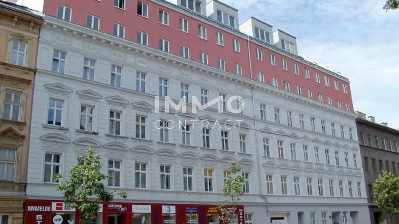 Historisches Gebäude mit einer modernen Dachaufstockung in urbaner Umgebung und Geschäften im Erdgeschoss.