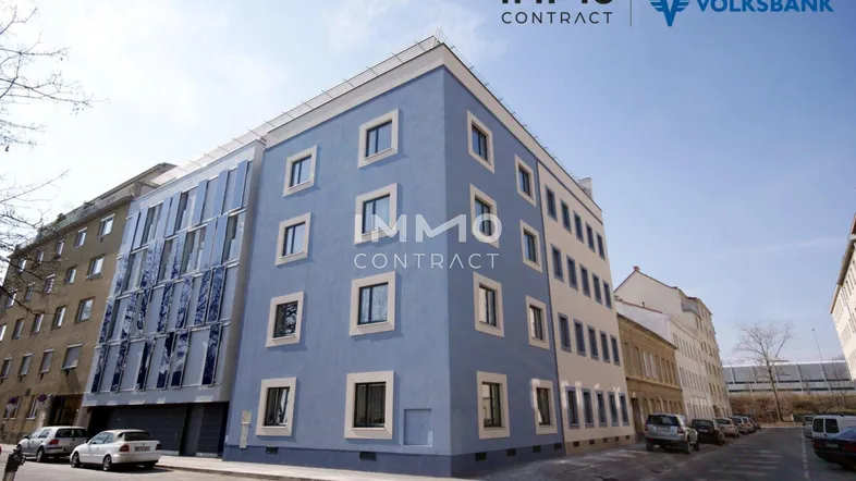 Neubau mit zeitgenössischer Architektur, blauer Fassade und Glasfront in urbaner Umgebung.