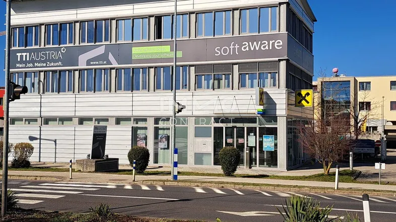 Modernes Bürogebäude mit großen Fensterfronten und Werbeschildern an einer belebten Straße.