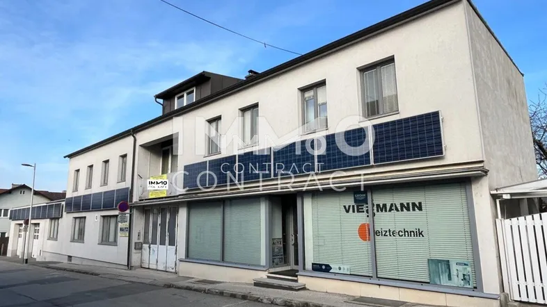 Gebäudeansicht von der Straße mit Solarpaneelen an der Fassade und Geschäftsflächen im Erdgeschoss.