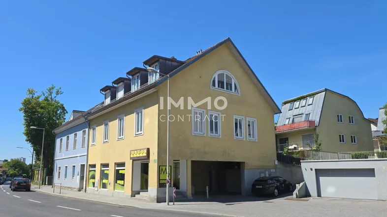 Gelbes Mehrfamilienhaus mit mehreren Fenstern und einem Garagenbereich an einer Straße gelegen.