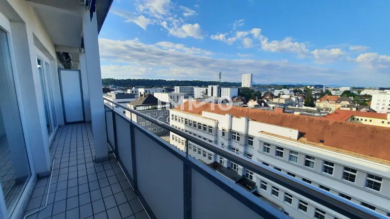 Geräumiger Balkon mit Fliesenboden und weitem Blick über die Stadtlandschaft unter blauem Himmel.