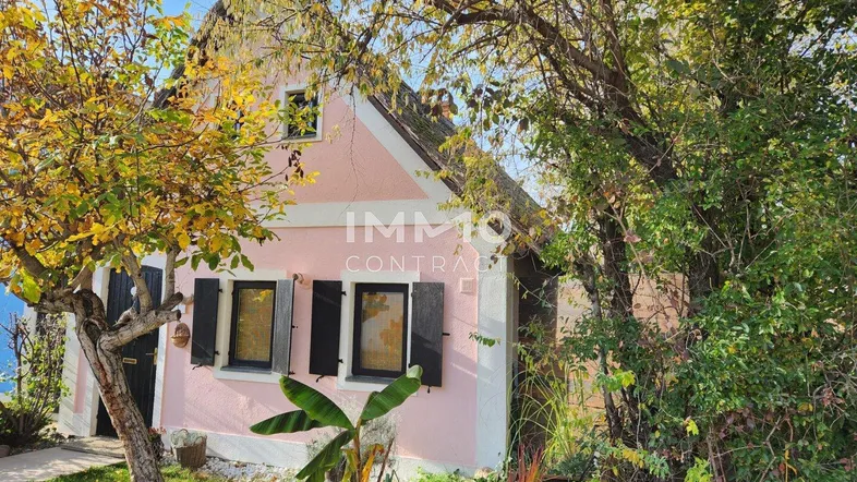 Charmantes rosa Haus mit grüner Umgebung und traditionellen Fensterläden unter blauem Himmel.