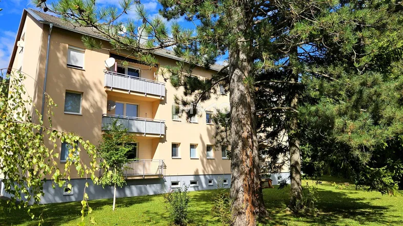 Mehrstöckiges Apartmentgebäude mit Balkonen, umgeben von Bäumen und Grünflächen.
