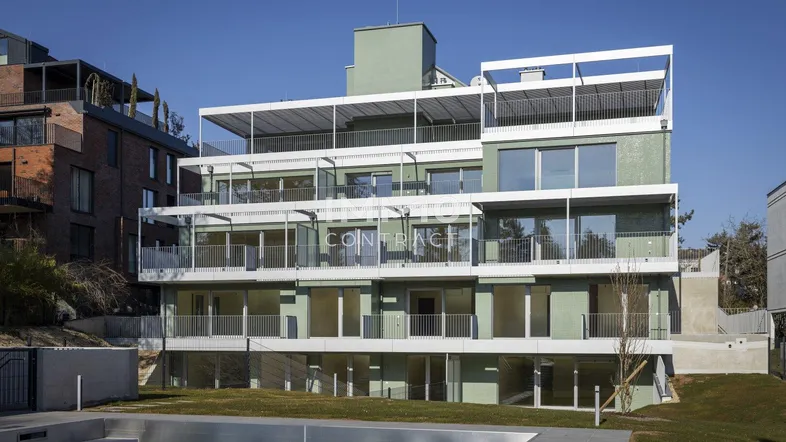 Modernes Apartmentgebäude mit mehreren Balkonen, großen Fenstern und einer gepflegten Grünfläche im Vordergrund.