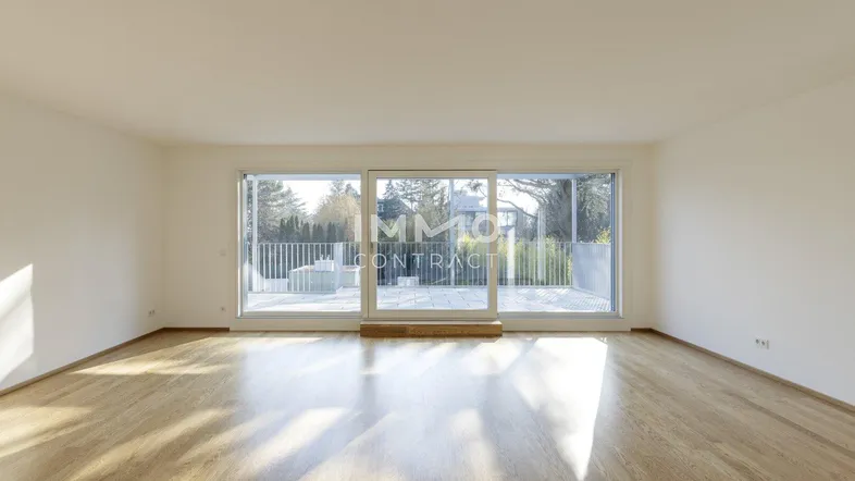 Helles, leeres Wohnzimmer mit Holzboden und Zugang zu einem großen Balkon.