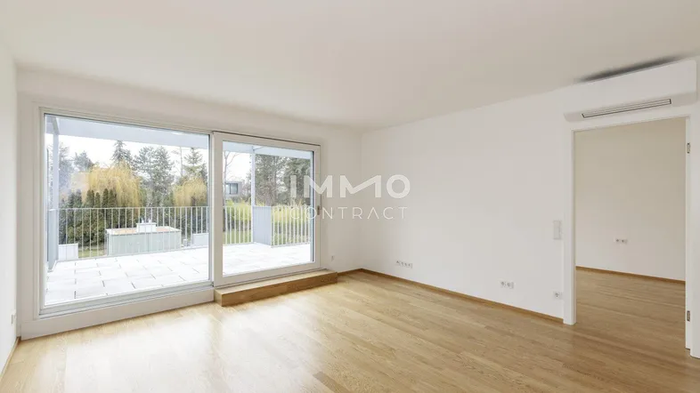 Helles Zimmer mit Holzboden, großen Schiebetüren und Zugang zu einer gefliesten Terrasse.