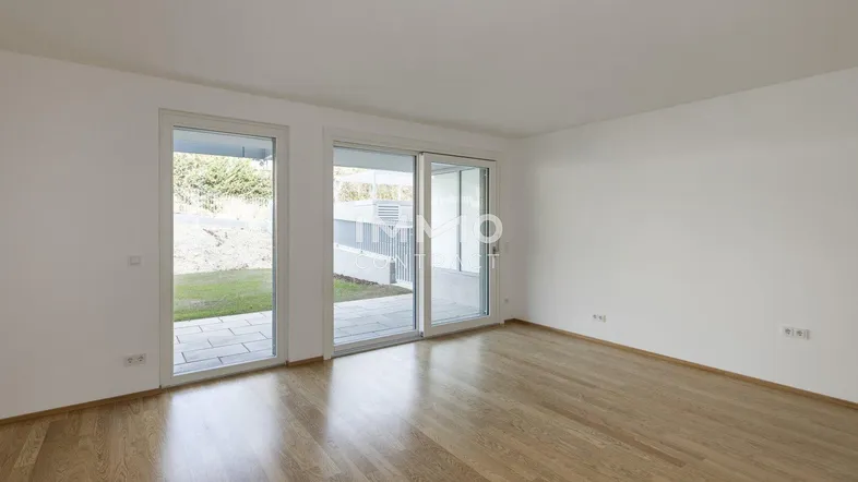 Helles, leeres Wohnzimmer mit Holzboden und Zugang zu einer Terrasse und dem Garten.