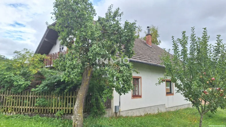 Ländliches Haus mit Satteldach und Gartenbereich, umgeben von Bäumen und grüner Landschaft.