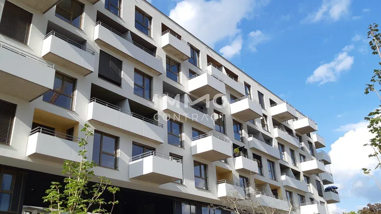 Moderne Wohnanlage mit vielen Balkonen und großen Fenstern unter blauem Himmel.