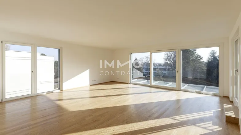 Helles, leeres Wohnzimmer mit großen Fenstern, Holzboden und viel natürlichem Licht.