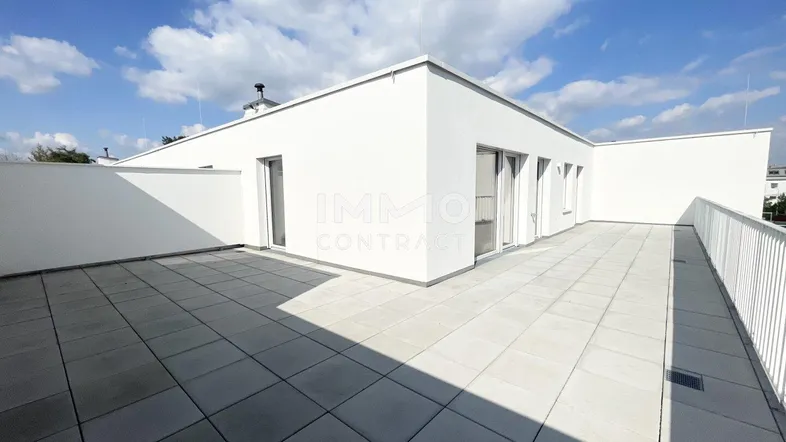 Geräumige Dachterrasse mit modernen weißen Wänden und Fliesenboden unter strahlend blauem Himmel.