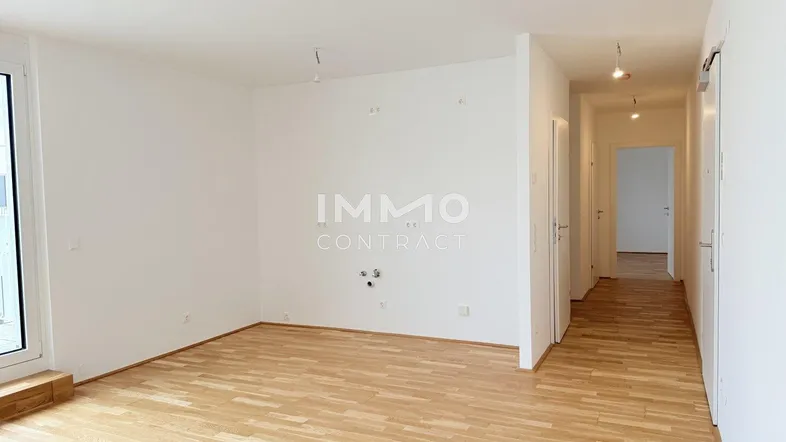 Helles, leeres Wohnzimmer mit Parkettboden und Zugang zu einem Außenbereich.