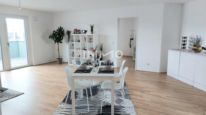 Heller offener Wohn-Essbereich mit Parkettboden, Esstisch und Zugang zu einem Balkon.