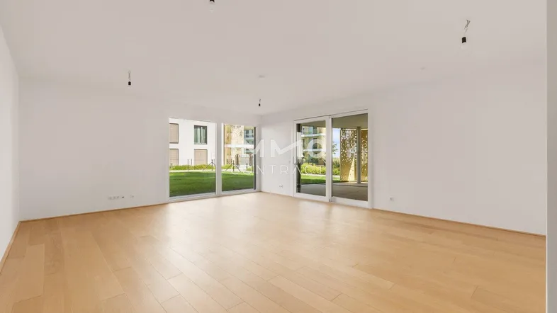 Helles, leeres Wohnzimmer mit Holzboden und großen Fenstern, die Zugang zum Garten bieten.
