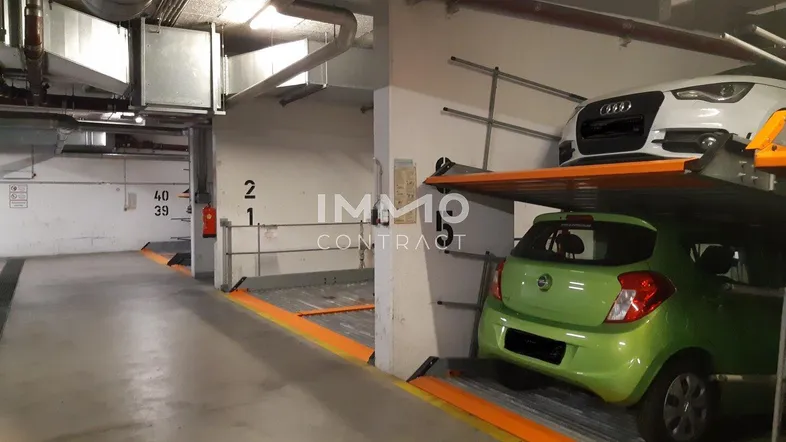 Tiefgarage mit modernem Doppelparker-System und sichtbaren Lüftungsrohren an der Decke.