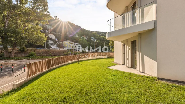 Moderne Wohnanlage mit gepflegtem Rasenbereich und Blick auf die umliegende Hügellandschaft bei Sonnenuntergang.