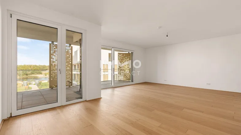Helles und geräumiges Wohnzimmer mit Holzboden und Zugang zu einem großen Balkon mit Seeblick.