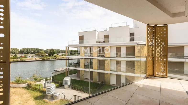 Geräumiger Balkon mit Fliesenboden und Glasgeländer bietet einen schönen Blick auf das Wasser und die moderne Architektur.