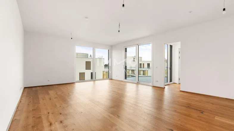 Geräumiges, helles Zimmer mit Holzboden und großen Fenstern, die viel Tageslicht hereinlassen.