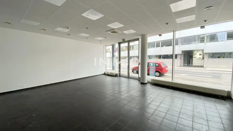 Geräumiger, leerer Geschäftsraum mit großen Schaufenstern und dunklen Fliesenböden, ideal für verschiedene Nutzungsmöglichkeiten.