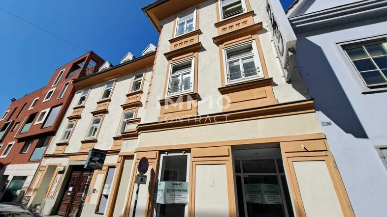 Historisches Gebäude mit mehreren Etagen und Geschäftsräumen im Erdgeschoss an einer städtischen Straße.