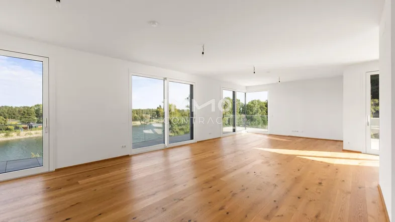 Helles, geräumiges Wohnzimmer mit Holzboden und großen Fenstern mit Blick auf den See.