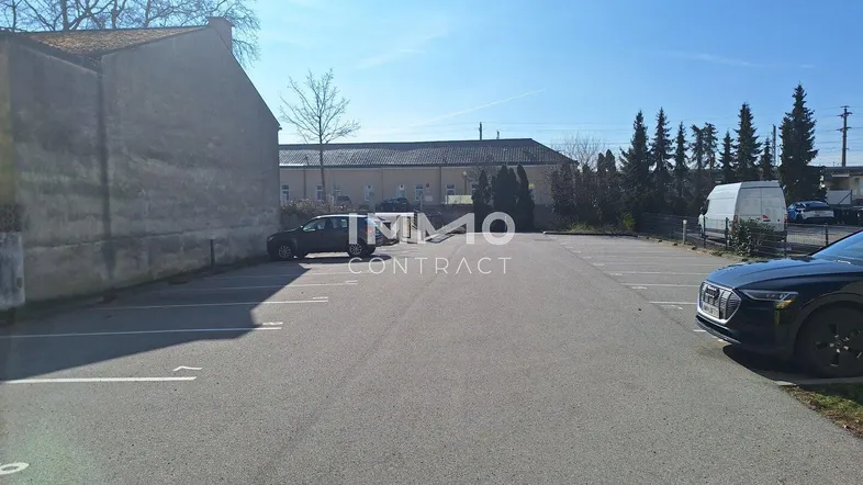 Großer asphaltierter Parkplatz mit markierten Stellplätzen und umliegenden Gebäuden unter blauem Himmel.