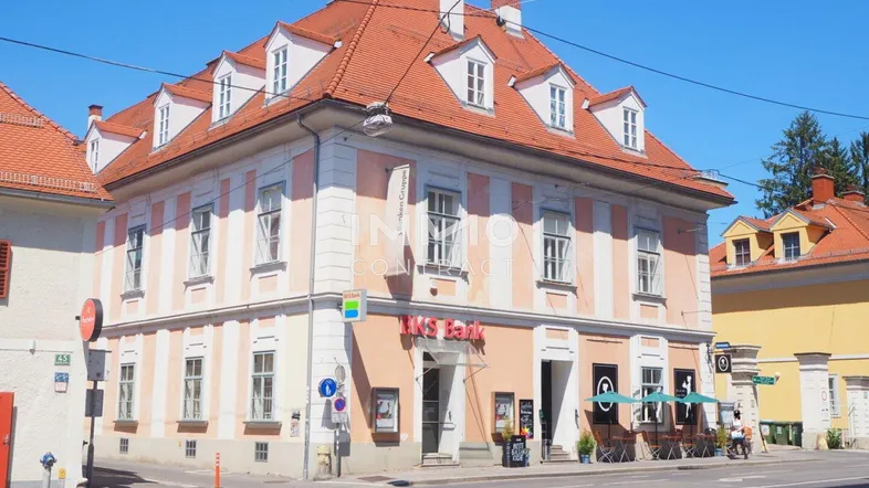 Historisches Gebäude mit orangerotem Dach und Geschäften im Erdgeschoss an einer belebten Straßenecke.
